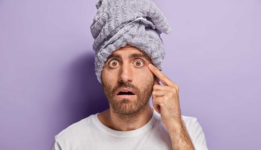 Un homme découvre qu'il a de l'acné sur le visage.